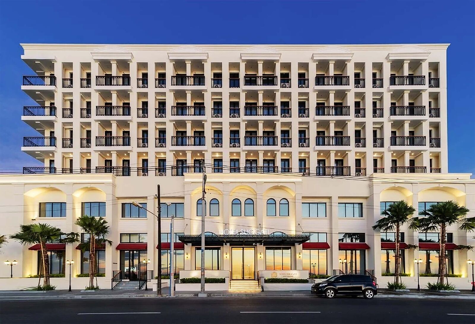 Front view of a white hotel with a columned entrance and red awnings