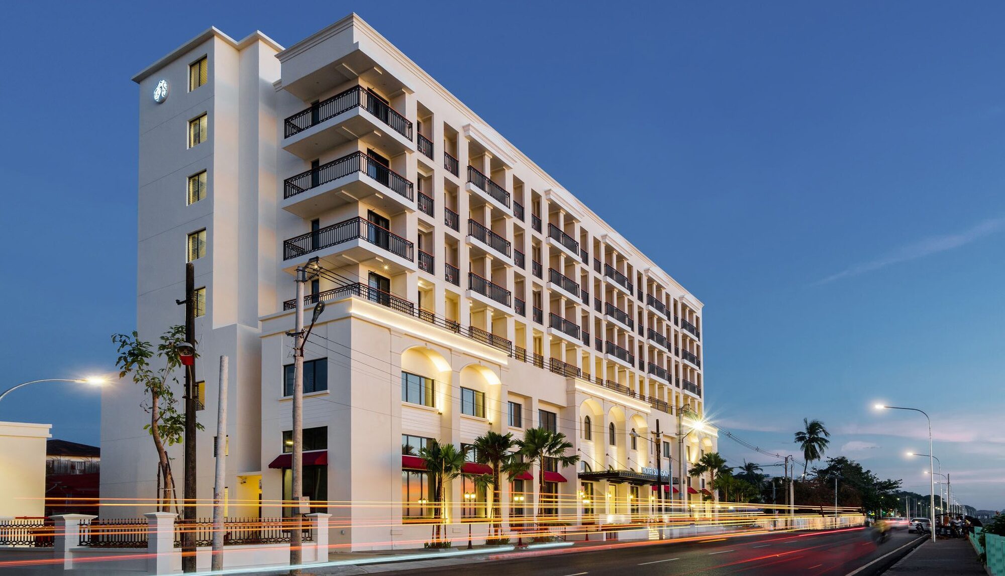 Hotel Suggati at dusk, a white riverside building with balconies and light trails along the road